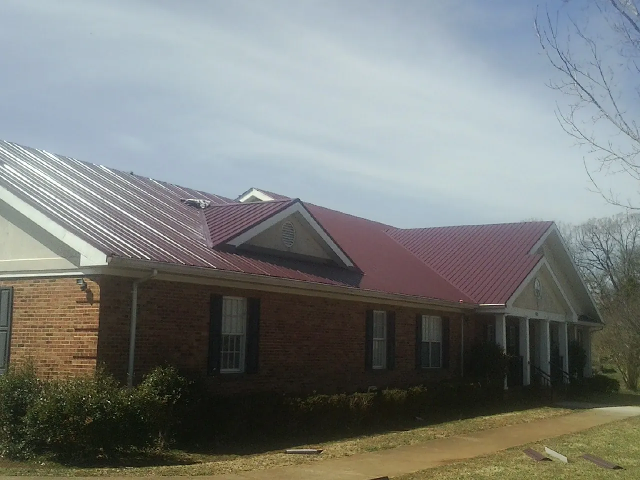 Red metal roof with gabled entries on a long brick building, from a Hail Damage Roof Repair job in Rippey