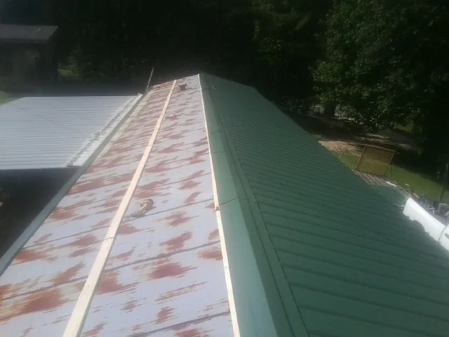 Old rusted panels beside newly installed green metal roofing — Wind Damage Roof Repair by Roofing Brothers in Rippey