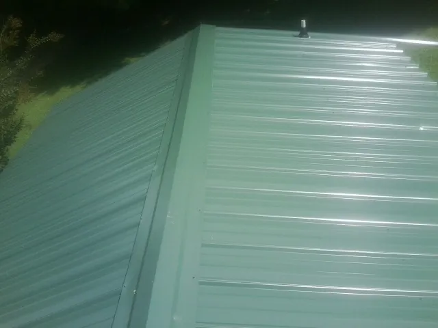 New green metal panels meeting at the ridge of a roof — Flat Roof Repair work by our crew in Rippey
