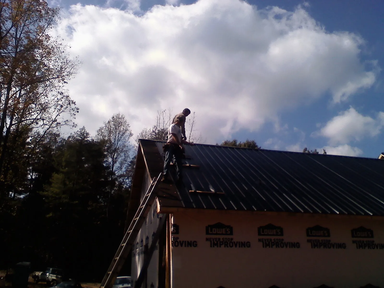 Roofer fastening dark metal panels high against a cloudy sky, from a Roof Inspection job in Rippey