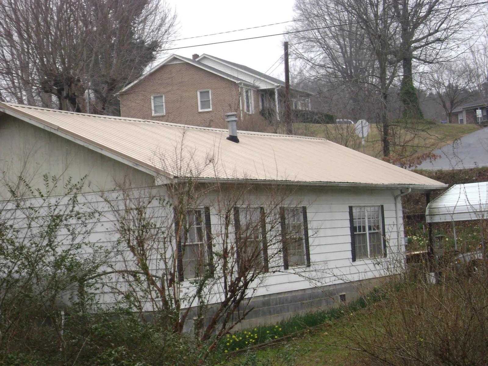 Tan metal roof on a white sided house set into a hillside — Commercial Roofing by Roofing Brothers in Rippey